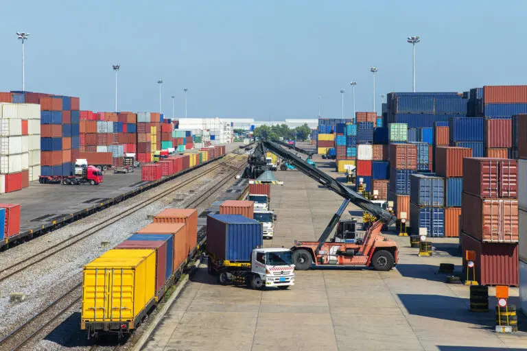 Busy shipping container yard with trucks and cranes handling cargo.