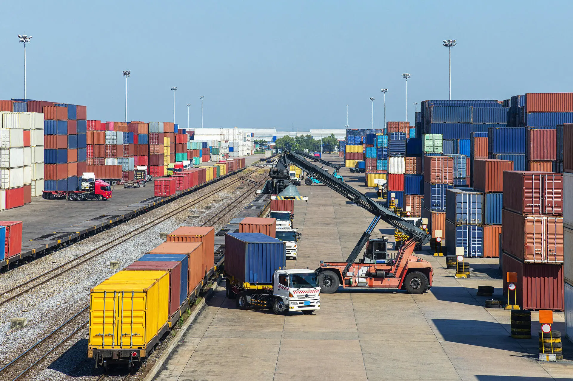 Busy shipping container yard with trucks and cranes handling cargo.